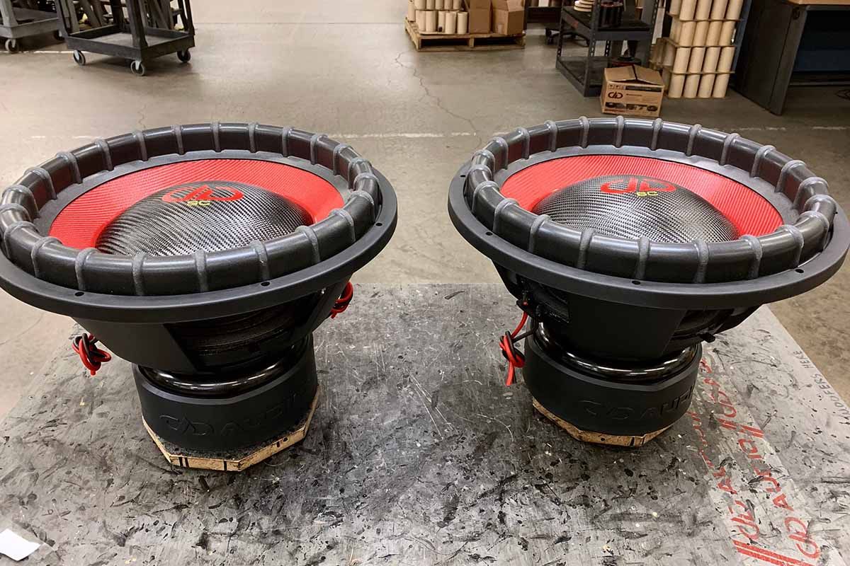 Two USA Made subwoofers with red cones, black carbon fiber dust caps, red DDA logos and yellow super charged decals