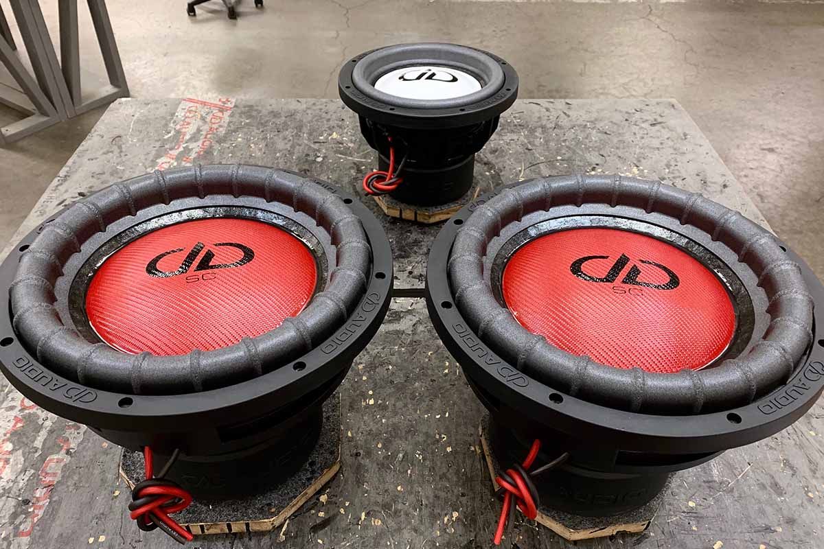 Two USA Made subwoofers with red carbon fiber dust caps, black DD classic logos and black super charged decals and one smaller USA made subwoofer with white epoxy dust cap and black DDA logo