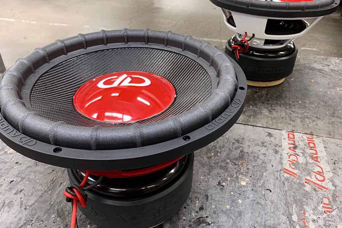 Two USA Made subwoofers - one with a red powder coat basket, black carbon fiber dust cap, red epoxy dust cap, white DDA logo, the other with a white powder coat basket and white DDA embossed logo
