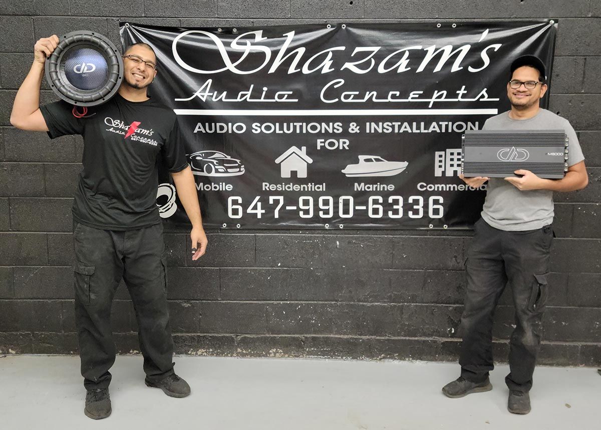 Shazam Audio Concepts - Staff holding Equipment in front of banner